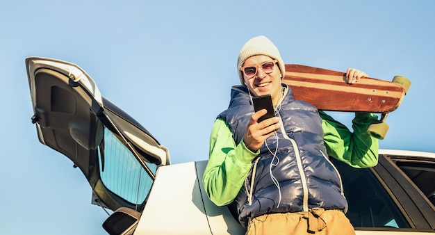 Hombre guapo joven inconformista con teléfono móvil inteligente escuchando música en viaje en coche