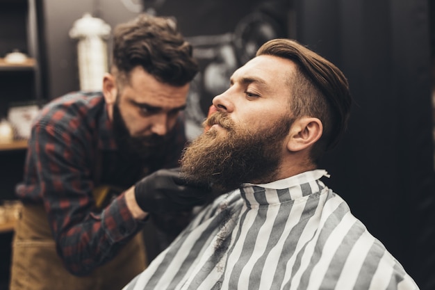 Hombre guapo joven inconformista visitando peluquería. Corte y peinado de barba a la moda y con estilo.