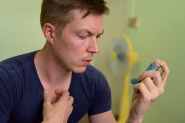 Hombre guapo joven con inhalador para el asma en casa