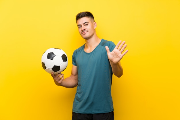 Foto hombre guapo joven jugador de fútbol saludando con la mano con expresión feliz