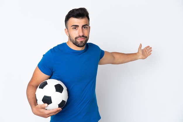 Hombre guapo joven jugador de fútbol sobre pared aislada extendiendo las manos hacia el lado para invitar a venir