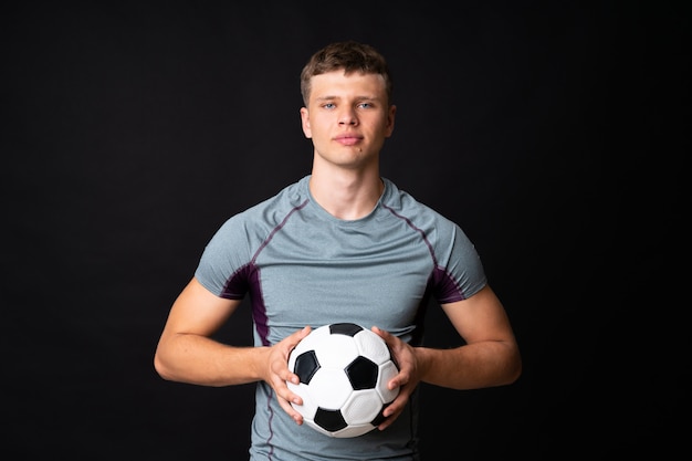 Hombre guapo joven jugador de fútbol sobre pared negra aislada