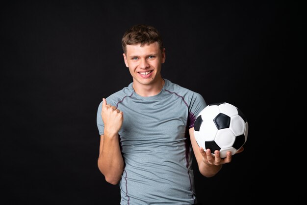 Hombre guapo joven jugador de fútbol sobre pared negra aislada