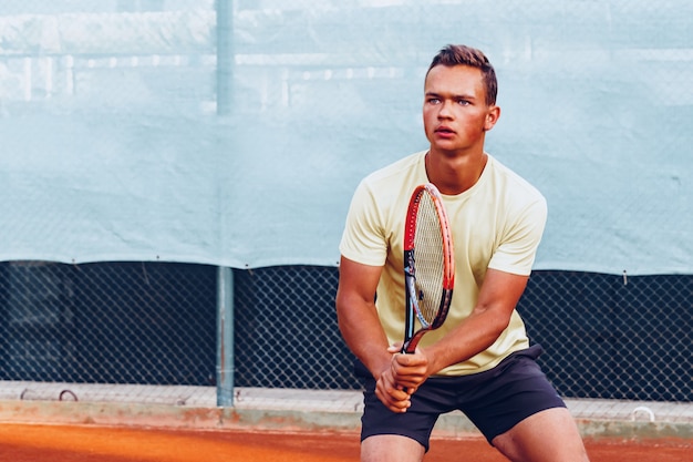 Hombre guapo joven jugando al tenis en la cancha de tenis