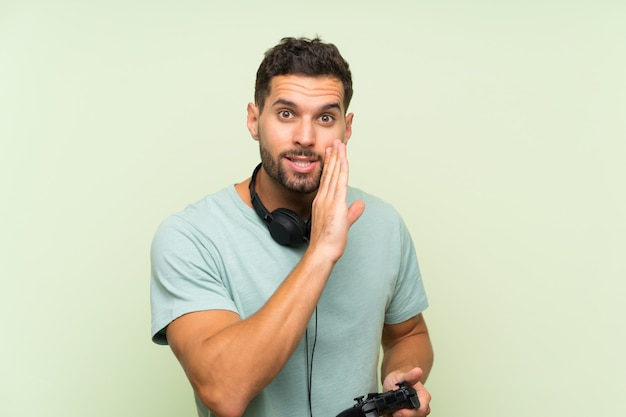 Foto hombre guapo joven jugando con un controlador de videojuego sobre pared verde aislado susurrando algo