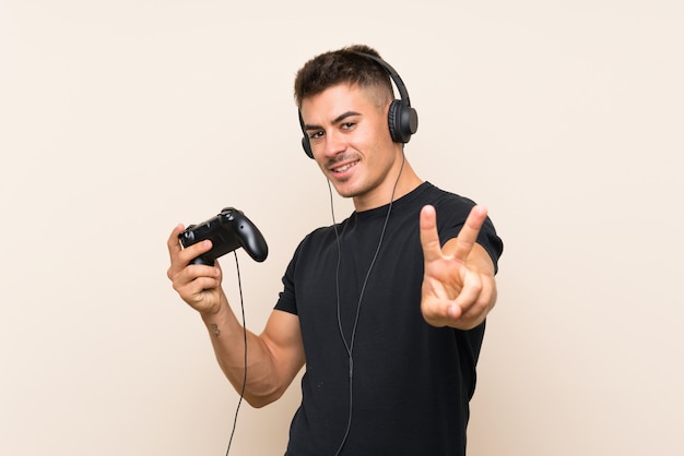 Hombre guapo joven jugando con un controlador de videojuego sonriendo y mostrando el signo de la victoria