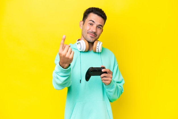 Hombre guapo joven jugando con un controlador de videojuegos sobre una pared aislada haciendo el gesto de venir