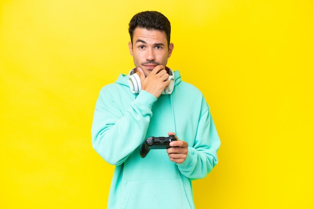 Hombre guapo joven jugando con un controlador de videojuegos sobre pensamiento de pared aislado