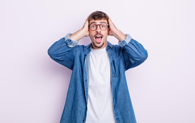 Hombre guapo joven levantando las manos a la cabeza, con la boca abierta, sintiéndose extremadamente afortunado, sorprendido, emocionado y feliz