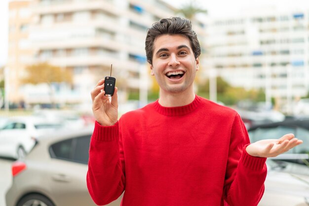 Hombre guapo joven con llave de coche con expresión facial sorprendida