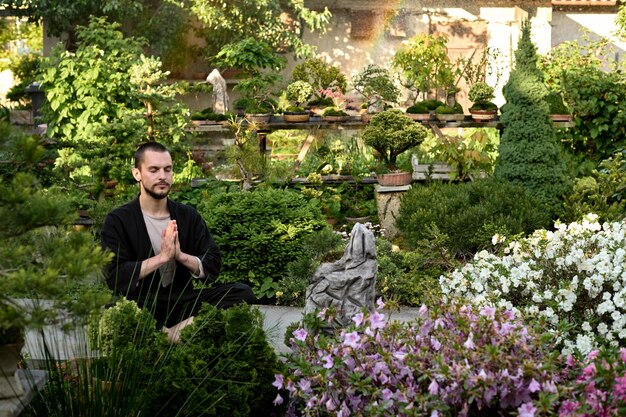 Hombre guapo joven meditando en el jardín de bonsai