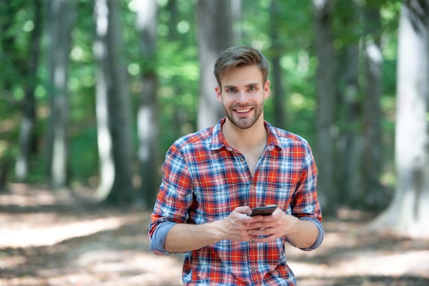 Hombre guapo joven en mensajes de camisa a cuadros en el teléfono al aire libre