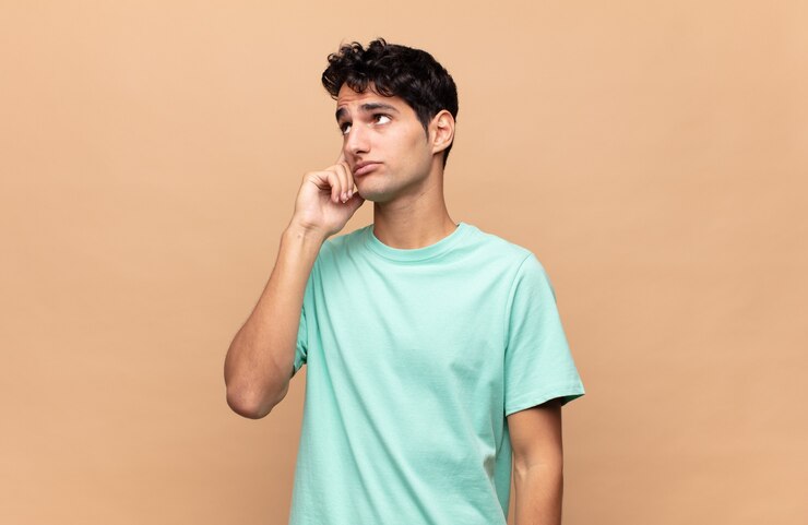 Foto hombre guapo joven con una mirada concentrada, preguntándose con una expresión dudosa, mirando hacia arriba y hacia un lado