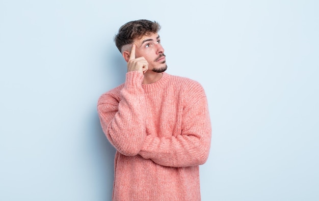 Hombre guapo joven con una mirada concentrada, preguntándose con una expresión dudosa, mirando hacia arriba y hacia un lado