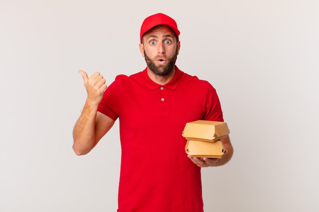 Hombre guapo joven mirando asombrado en concepto de entrega de hamburguesa de incredulidad