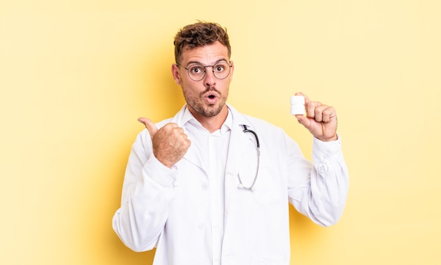 Hombre guapo joven mirando asombrado con incredulidad. concepto de botella de píldoras médico