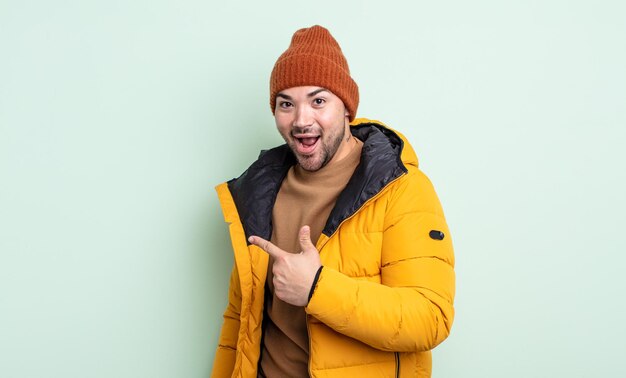 Hombre guapo joven mirando emocionado y sorprendido apuntando hacia un lado. concepto de clima frío