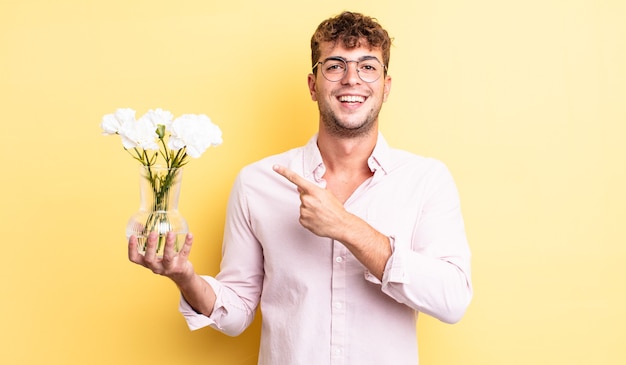 Hombre guapo joven mirando emocionado y sorprendido apuntando hacia un lado. concepto de flores