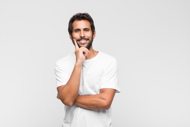 Hombre guapo joven mirando feliz y sonriendo con la mano en la barbilla