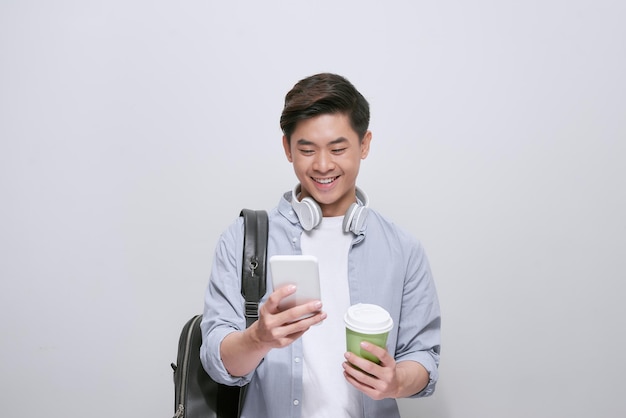 Hombre guapo joven con mochila con teléfono inteligente y café. Estudiante sonriente yendo de viaje. aislado sobre fondo blanco