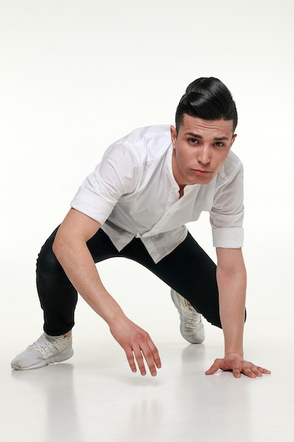 Hombre guapo, joven y moderno está sentado en el suelo en estudio sobre fondo gris. Hombre guapo sentado