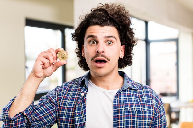 Foto hombre guapo joven con una moneda de bitcoin en el interior de casa