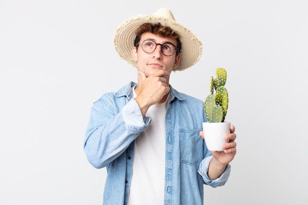 Hombre guapo joven pensando, sintiéndose dudoso y confundido. granjero sosteniendo un cactus decorativo