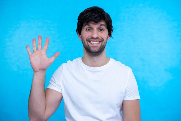 Hombre guapo joven de pie mostrando y apuntando hacia arriba con los dedos número cinco mientras sonríe confiado y feliz