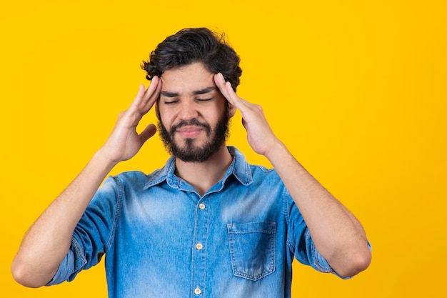 Hombre guapo joven de pie sobre un fondo amarillo aislado que sufre de dolor de cabeza desesperado y estresado por el dolor y la migraña Manos en la cabeza