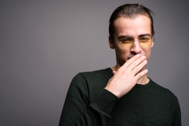 Hombre guapo joven que cubre la boca en estudio gris