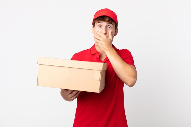 Hombre guapo joven que cubre la boca con las manos con un concepto de servicio de paquete de entrega conmocionado.