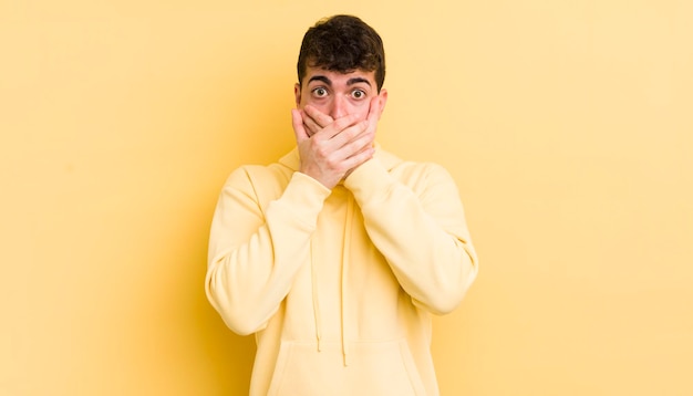 Hombre guapo joven que cubre la boca con las manos con una expresión sorprendida sorprendida guardando un secreto o diciendo uy