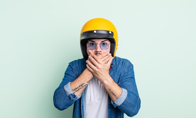 Hombre guapo joven que cubre la boca con las manos con una sorpresa. concepto de casco de moto