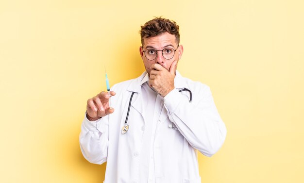 Hombre guapo joven que cubre la boca con las manos con una sorpresa. concepto de jeringa médico