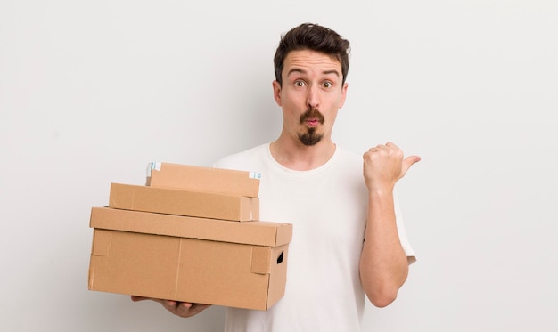 Hombre guapo joven que parece asombrado por el concepto de cajas de envío de incredulidad