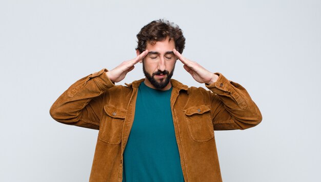 Hombre guapo joven que parece concentrado, pensativo e inspirado, haciendo una lluvia de ideas e imaginando con las manos en la frente contra la pared plana