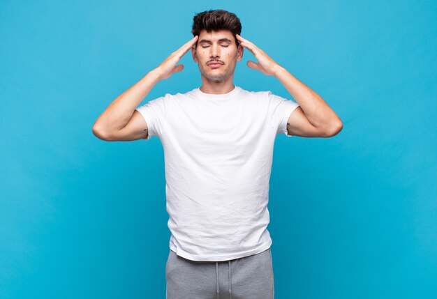 Foto hombre guapo joven que parece concentrado, reflexivo e inspirado, haciendo una lluvia de ideas e imaginando con las manos en la frente