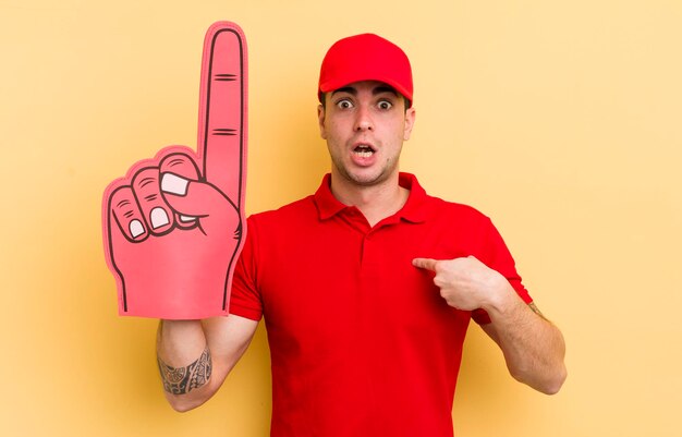 Hombre guapo joven que parece conmocionado y sorprendido con la boca abierta apuntando al concepto de mano número uno