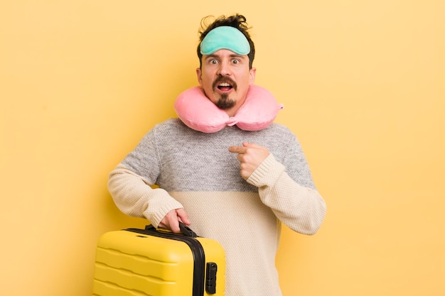 Hombre guapo joven que parece conmocionado y sorprendido con la boca abierta apuntando al concepto de pasajero de viaje propio