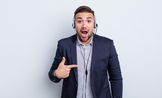 Hombre guapo joven que parece conmocionado y sorprendido con la boca abierta, apuntándose a sí mismo. concepto de telemarketer