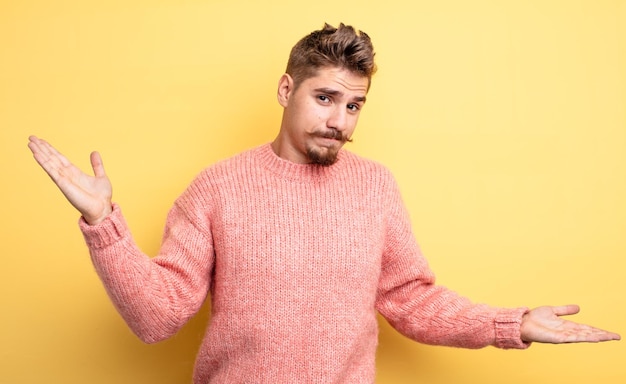 Hombre guapo joven que parece desconcertado, confundido y estresado, preguntándose entre diferentes opciones, sintiéndose inseguro. extraño concepto de bigote