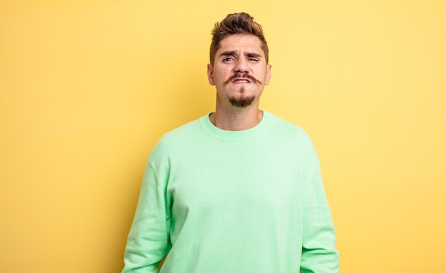 Hombre guapo joven que parece desconcertado y confundido, mordiendo el labio con un gesto nervioso, sin saber la respuesta al problema. extraño concepto de bigote