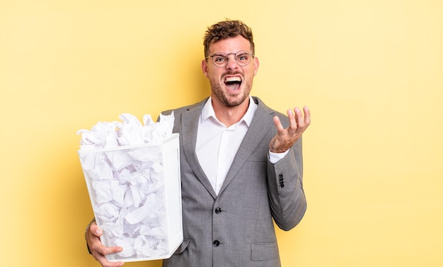 Hombre guapo joven que parece desesperado concepto de basura de bolas de papel frustrado y estresado