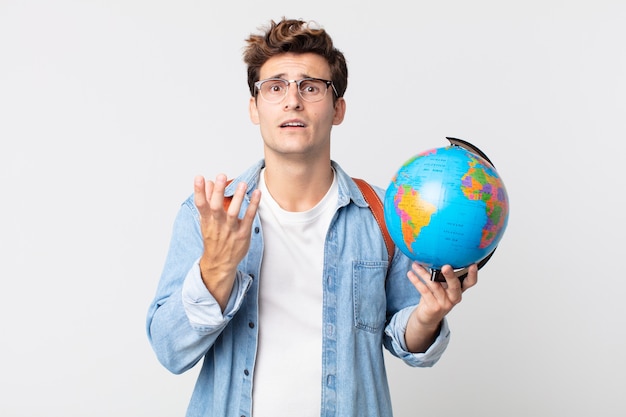 Hombre guapo joven que parece desesperado, frustrado y estresado. estudiante sosteniendo un mapa del globo terráqueo