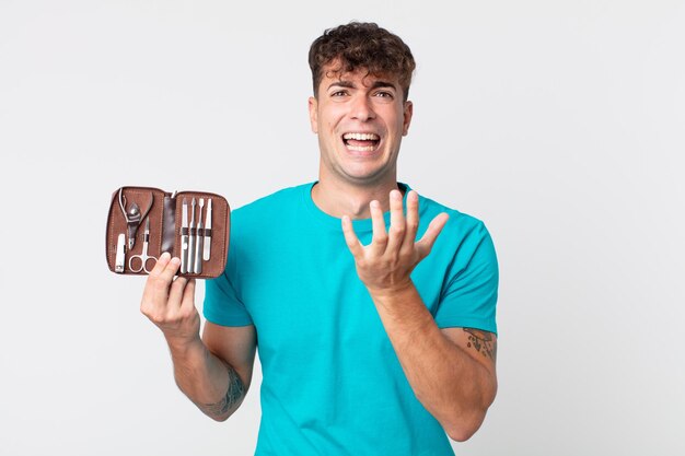 Hombre guapo joven que parece desesperado, frustrado y estresado y sosteniendo una caja de herramientas de uñas