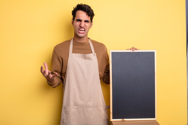 Hombre guapo joven que parece enojado, molesto y frustrado. concepto de chef y pizarra