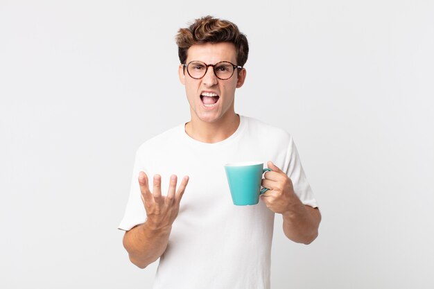 Hombre guapo joven que parece enojado, molesto y frustrado y sosteniendo una taza de café