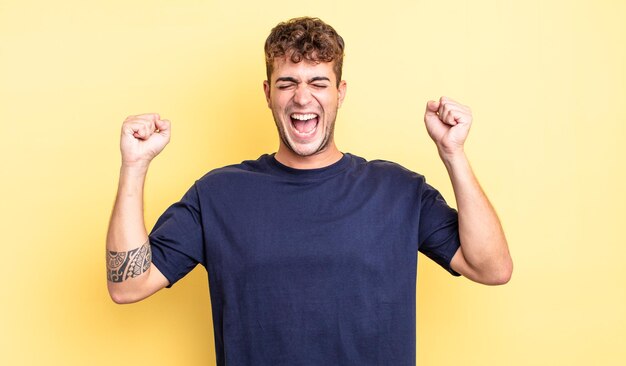 Hombre guapo joven que parece extremadamente feliz y sorprendido celebrando el éxito gritando y saltando