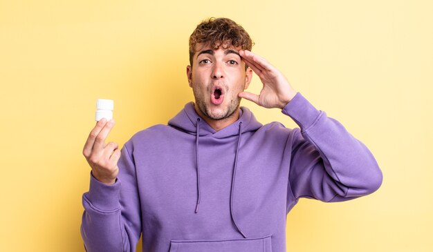 Hombre guapo joven que parece feliz, asombrado y sorprendido. concepto de botella de pastillas