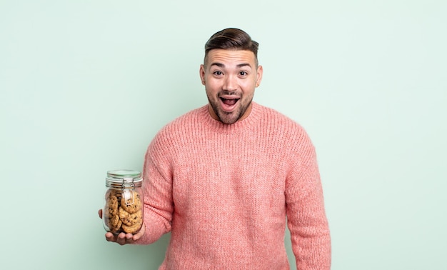 Hombre guapo joven que parece feliz y gratamente sorprendido. concepto de botella de galletas